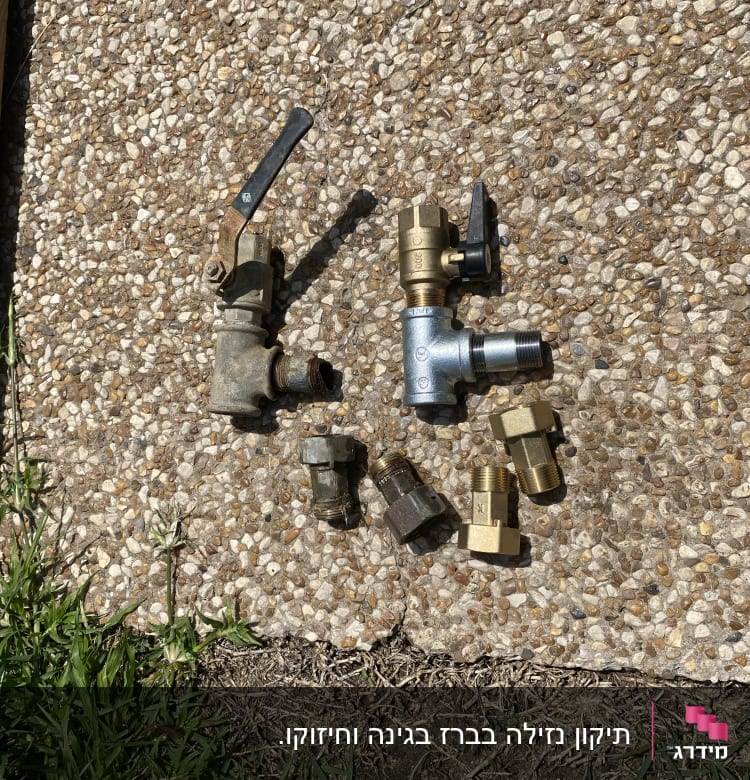 חלקי צנרת מתכתיים על משטח חצץ